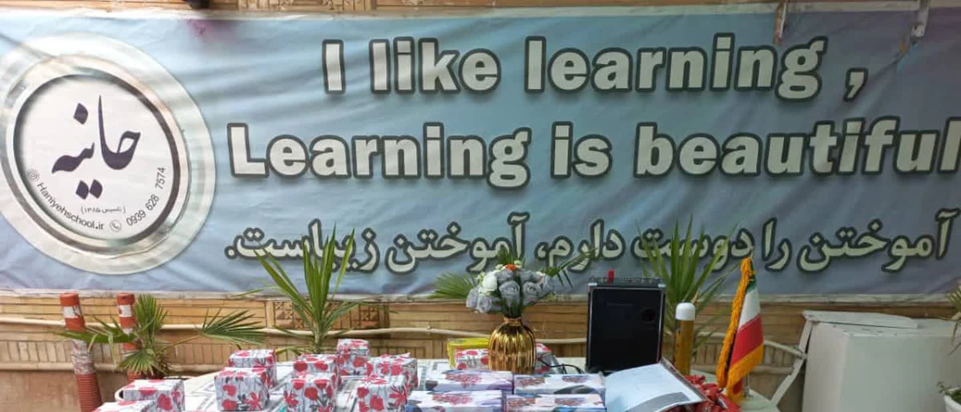 میز خوش‌آمدگویی با بنر «آموختن را دوست دارم» و نشان مجتمع آموزشی حانیه